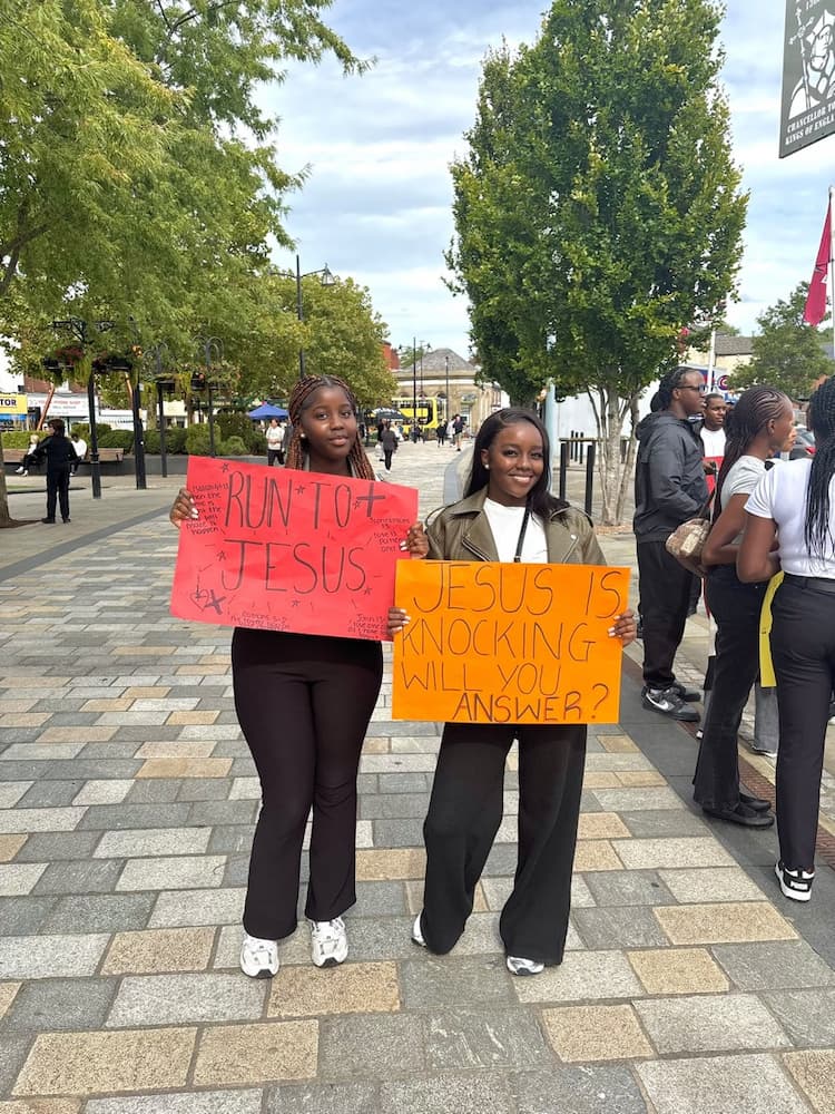 Two young women holding colourful signs about Jesus during street mission